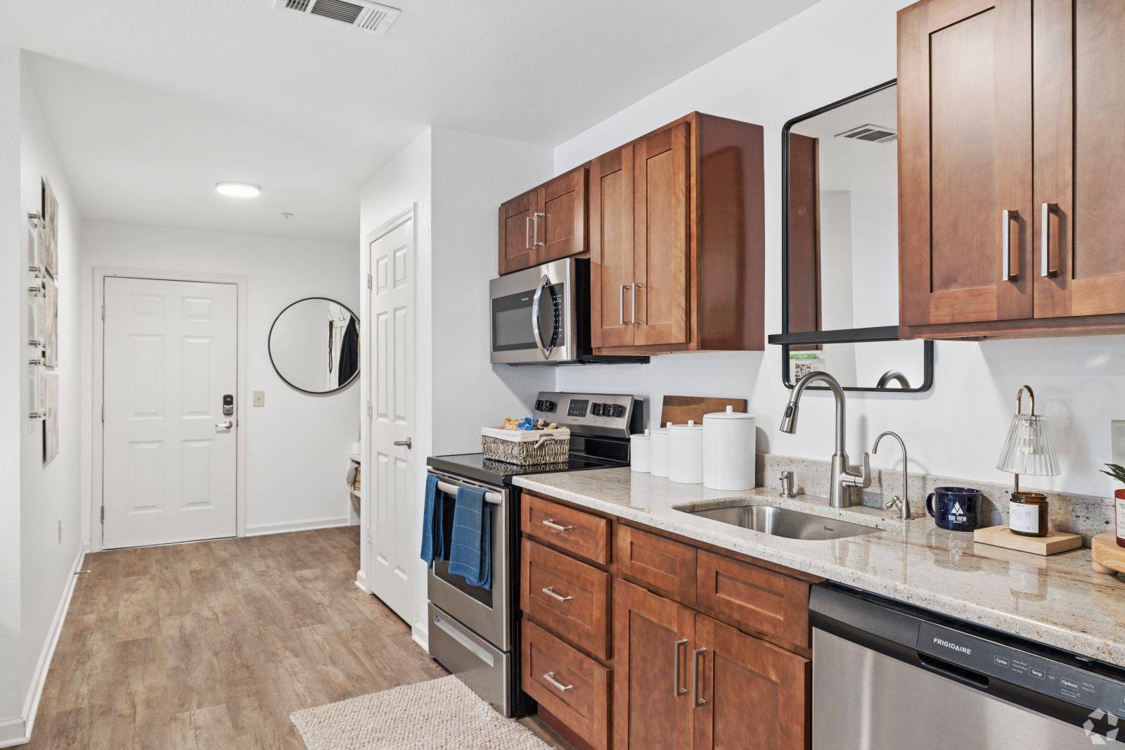 Apartment entryway opening into a kitchen with wood cabinets, granite counters, and stainless steel appliances