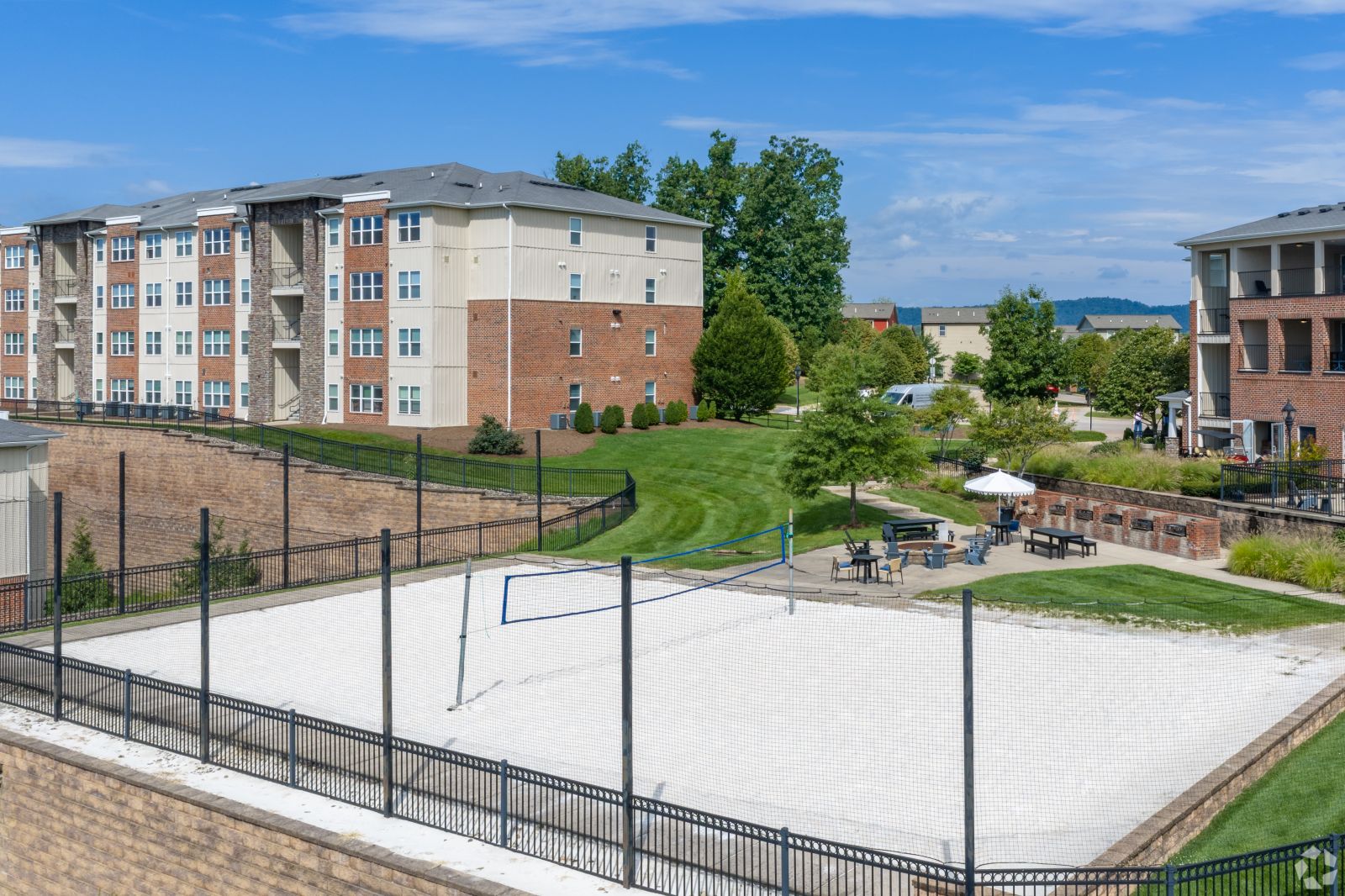 Sand volleyball court and outdoor seating area surrounded by apartment buildings and landscaped lawns