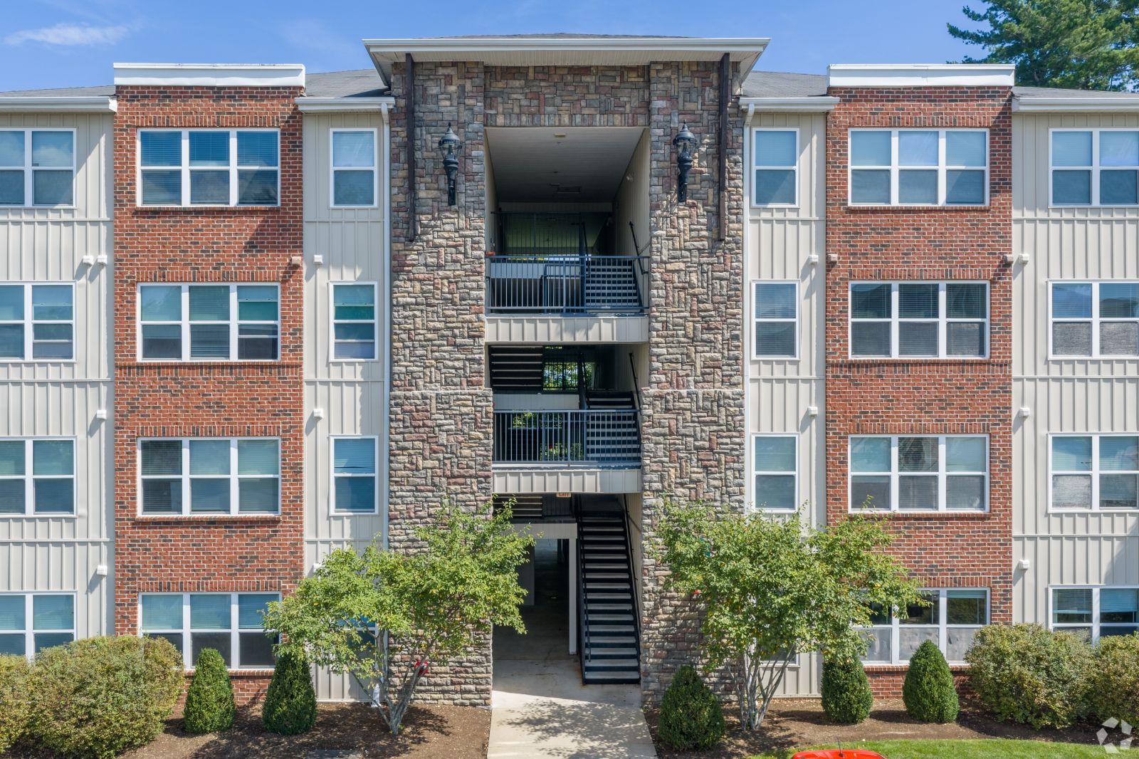 Front of a four-story apartment building with brick, gray siding, balconies, and a central staircase