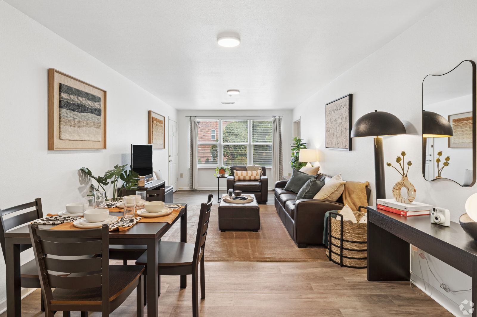 Open-plan apartment dining and living area with dark wood furniture, a sofa, and large windows
