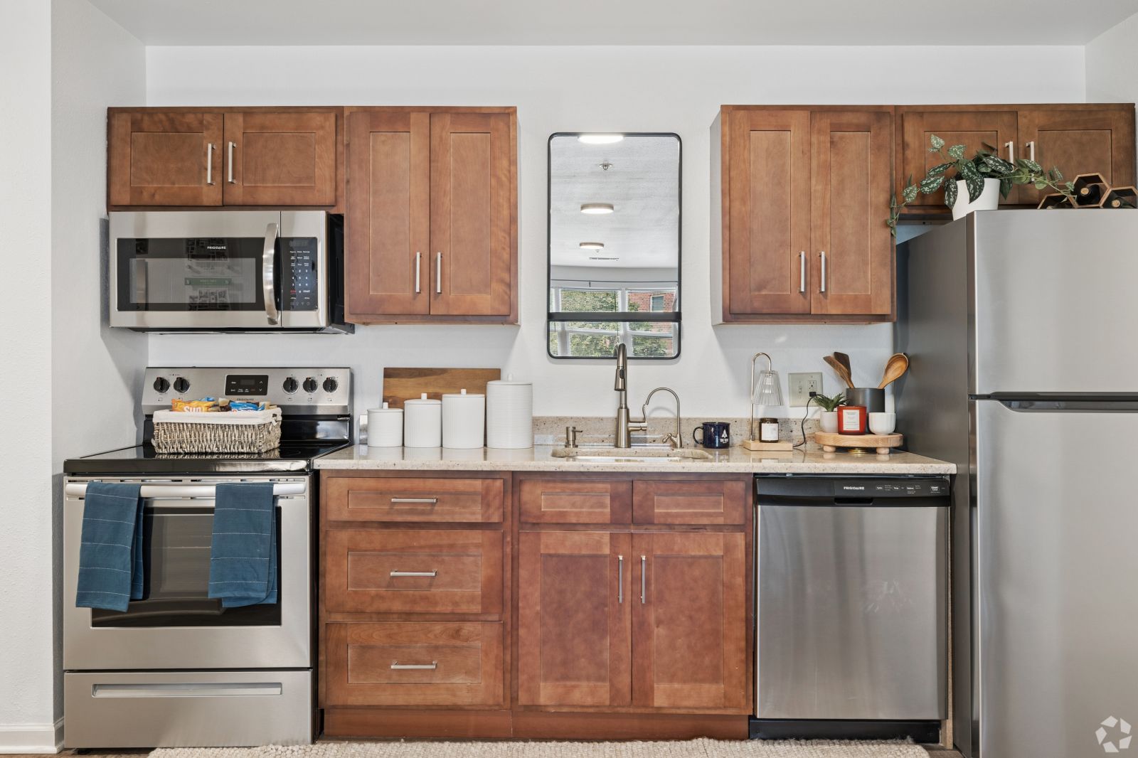 Apartment kitchen with wood cabinets, granite counters, stainless steel appliances, and a window above the sink