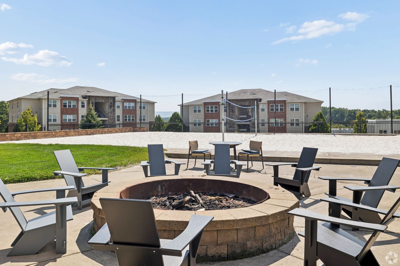 Outdoor stone fire pit surrounded by Adirondack chairs with apartment buildings in the background