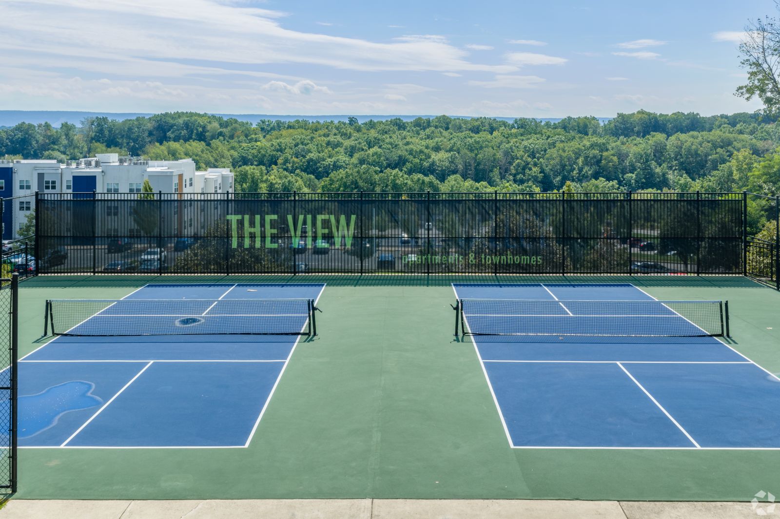 The-View_015 Two outdoor tennis courts with blue playing surfaces and “The View” displayed on the perimeter fence