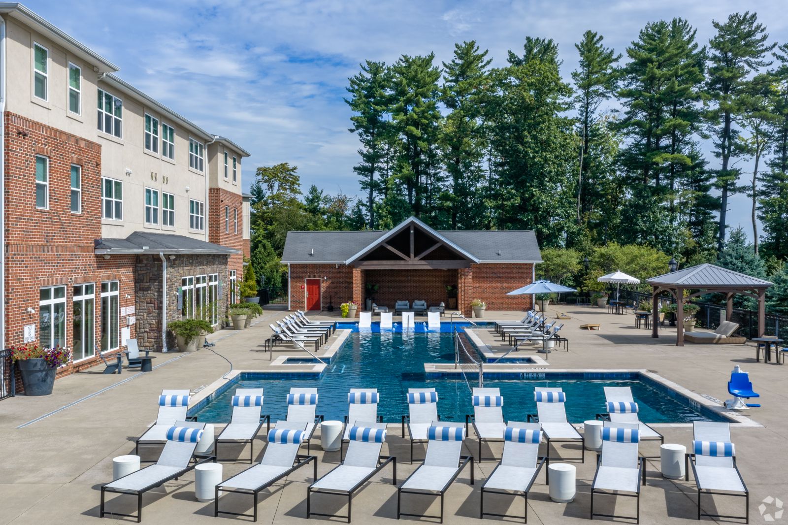 Outdoor swimming pool with striped lounge chairs, cabanas, and a brick clubhouse