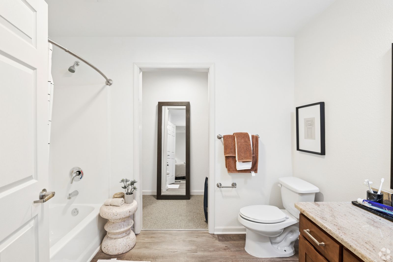 Bright bathroom with a tub and shower, toilet, vanity, towel rack, and full-length mirror